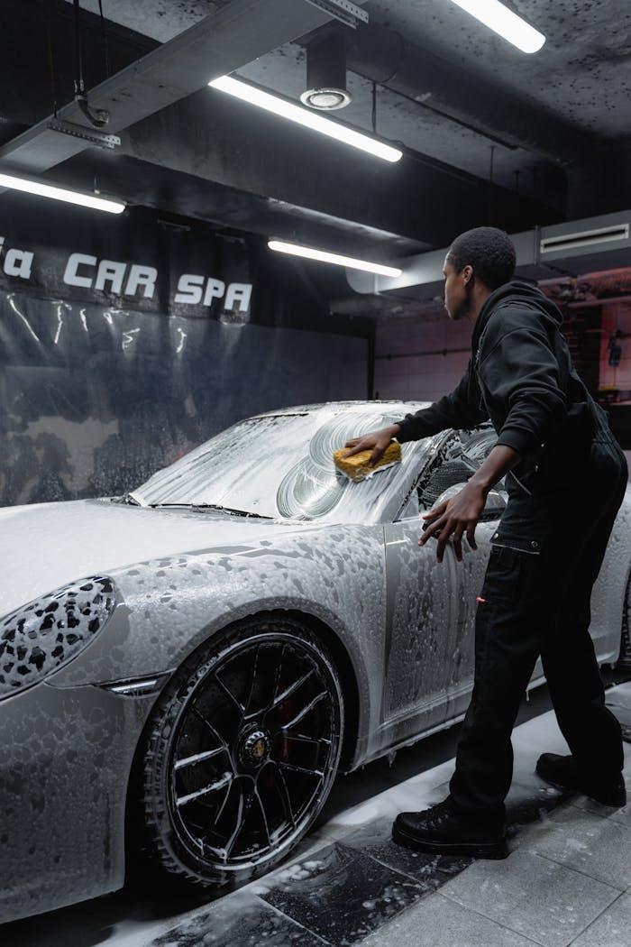 services-03 Employee in uniform cleaning a luxury car with foam at an indoor car spa.