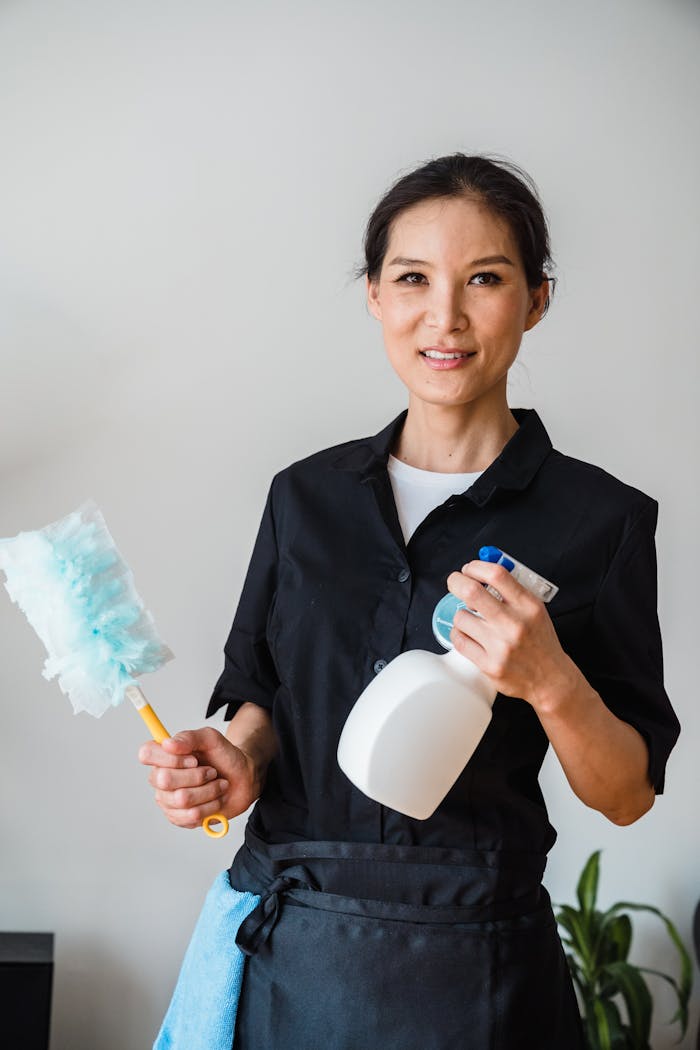 why-choose-us A female housekeeper smiling while holding cleaning tools indoor.