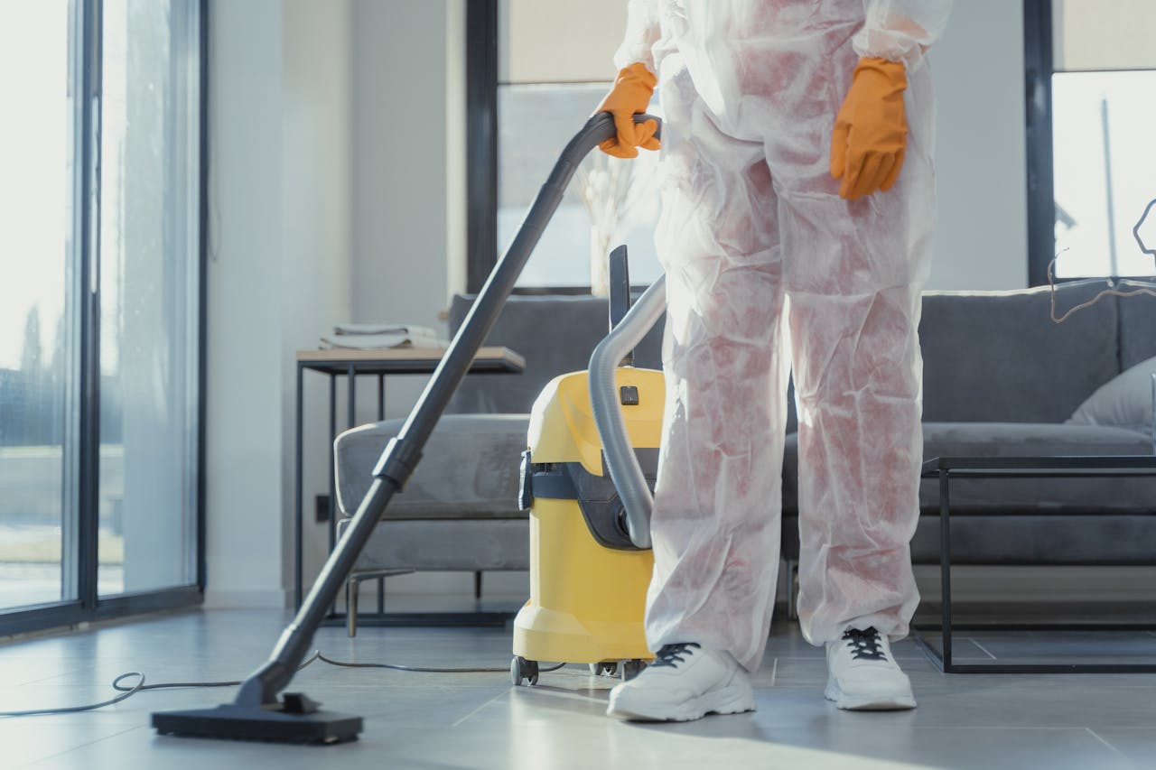 gallery-1 A cleaner in protective coveralls and gloves vacuuming a modern living room.